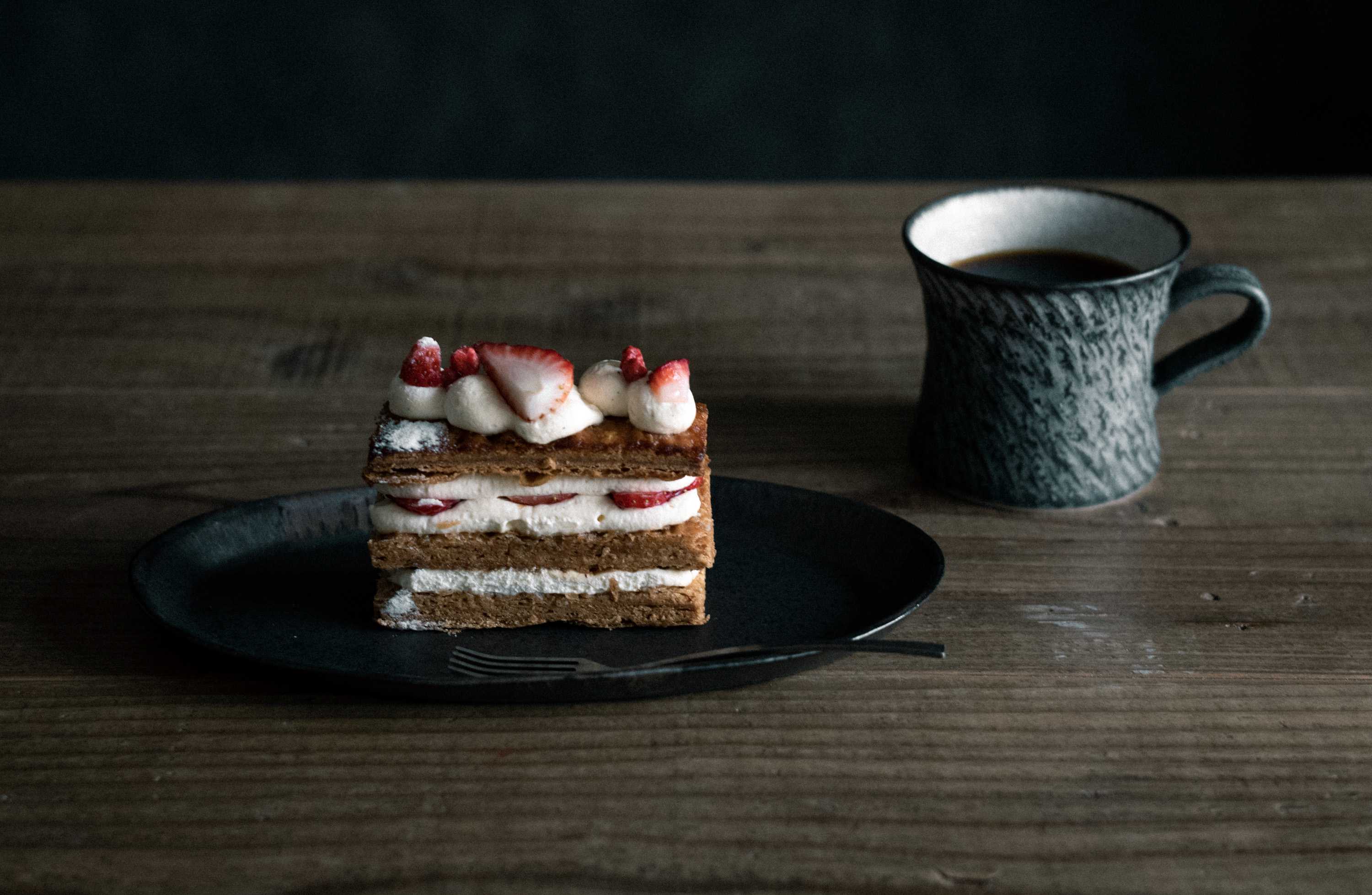 KODAMA TOKIさんの黒い器に盛ったいちごのミルフィーユパイと陶器のカップのある食卓